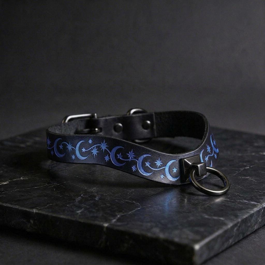 A black leather collar with a silver metal ring and blue star-and-crescent pattern on it, resting on a dark surface.