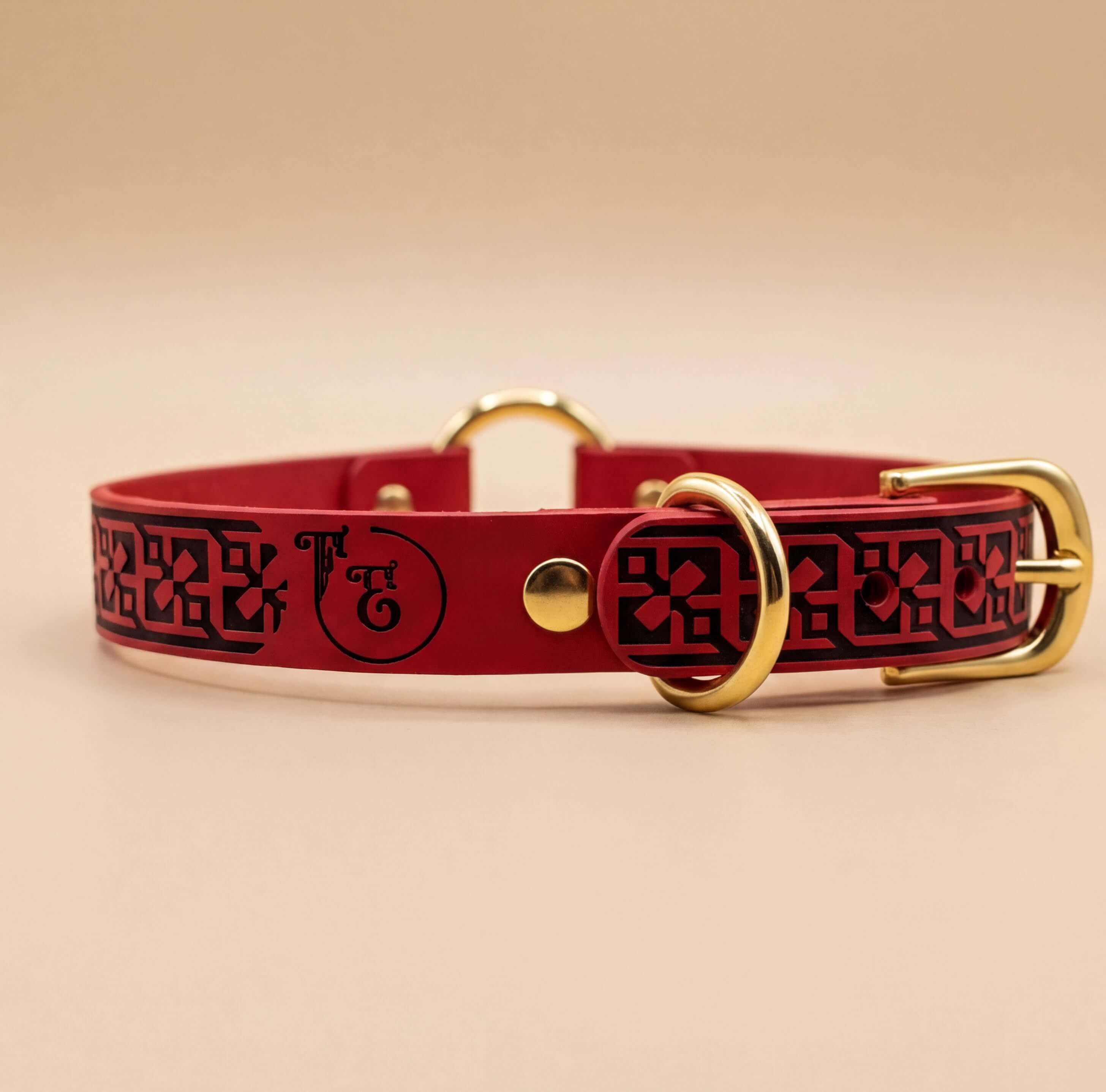 A red leather dog collar with a gold buckle and a black geometric pattern.