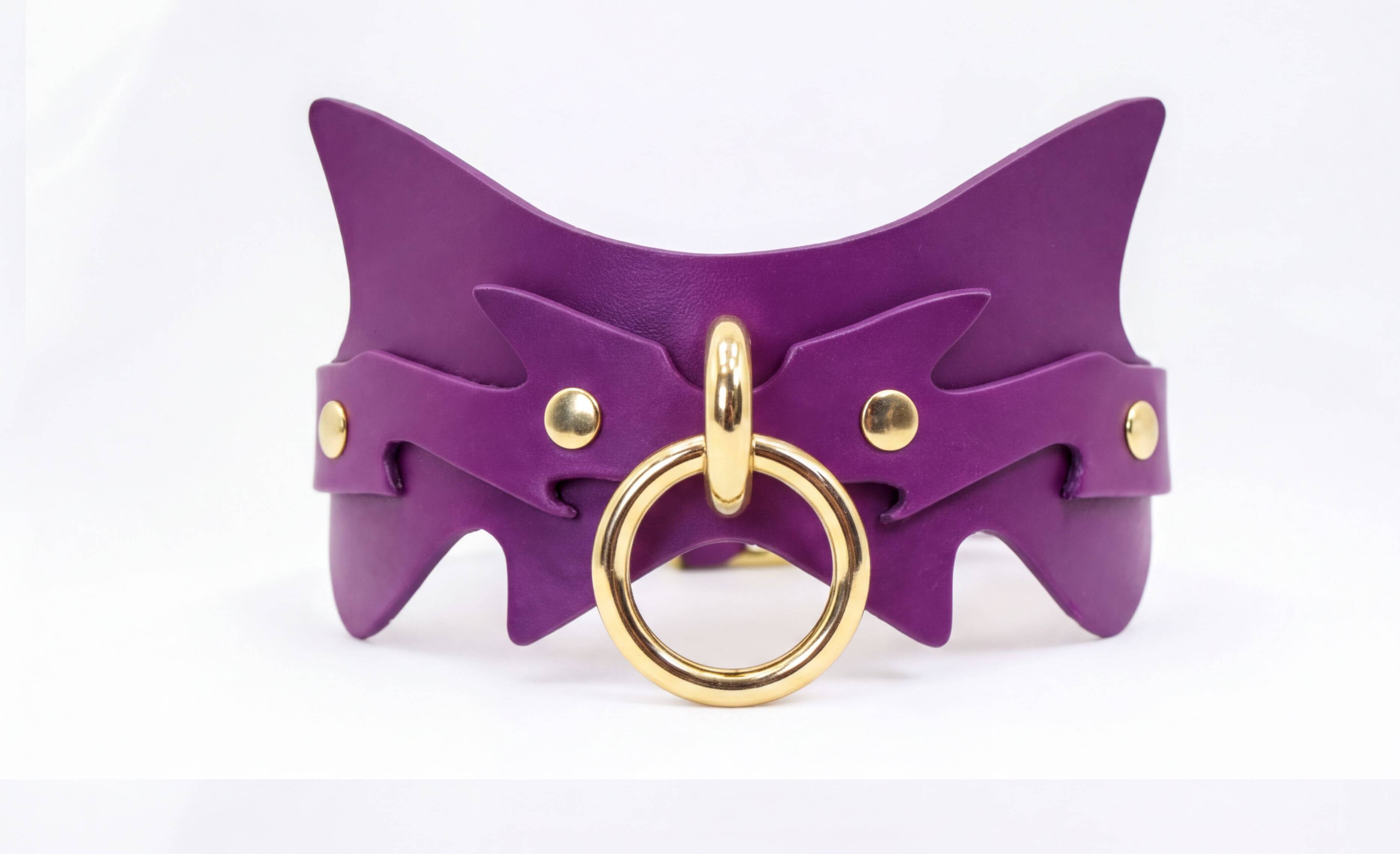A purple leather choker necklace with a gold ring and two gold studs on the sides.