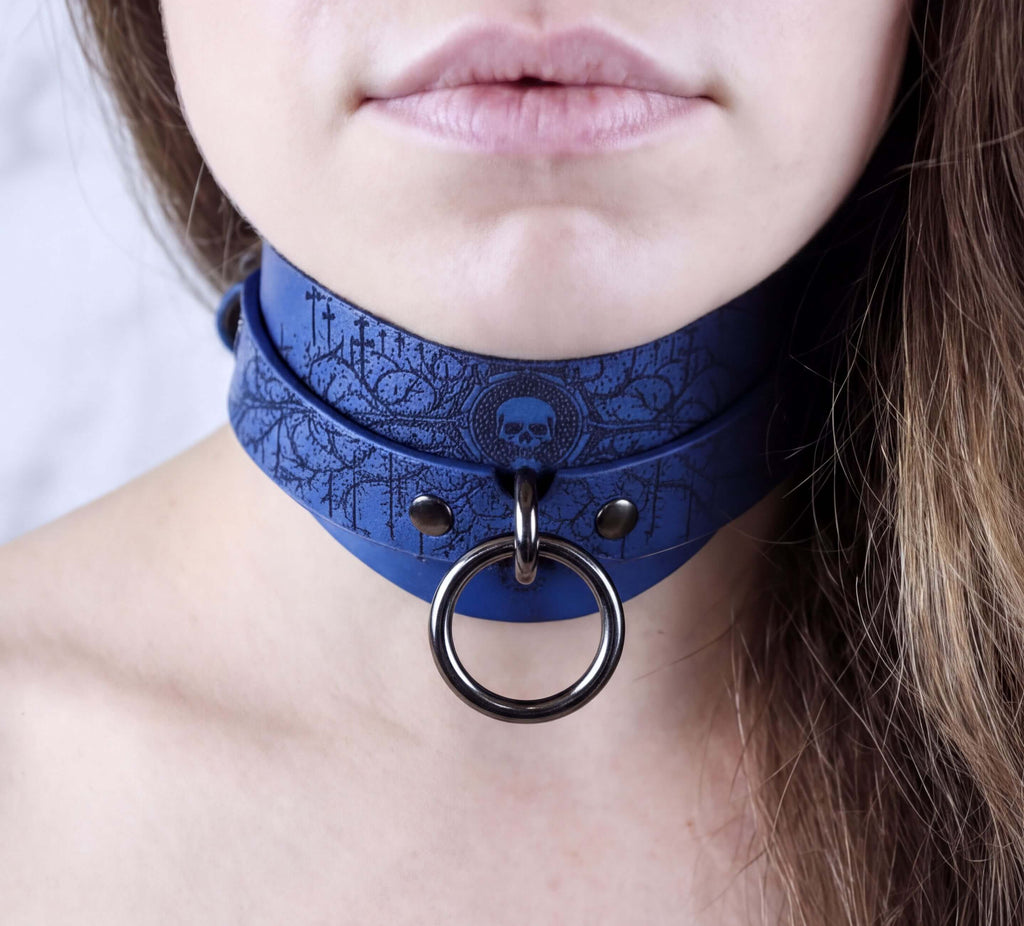 A close-up of a person's neck and chin wearing a blue choker necklace with a skull design and a metal ring.