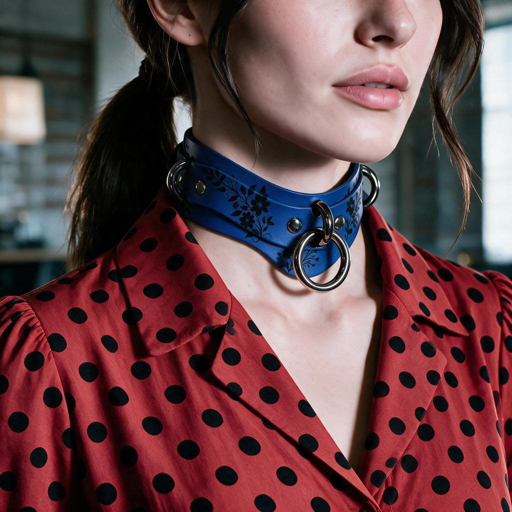 A close-up of a woman wearing a blue choker necklace with metal rings, paired with a red polka-dot blouse.