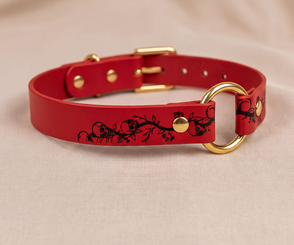 A red leather collar with a gold-colored buckle and a black floral design on the strap.