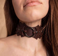 A close-up of a woman's neck and chin wearing a brown leather choker necklace with a circular metal ring.