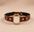 A brown leather choker collar with a gold-colored circular loop and two heart-shaped holes on the sides.