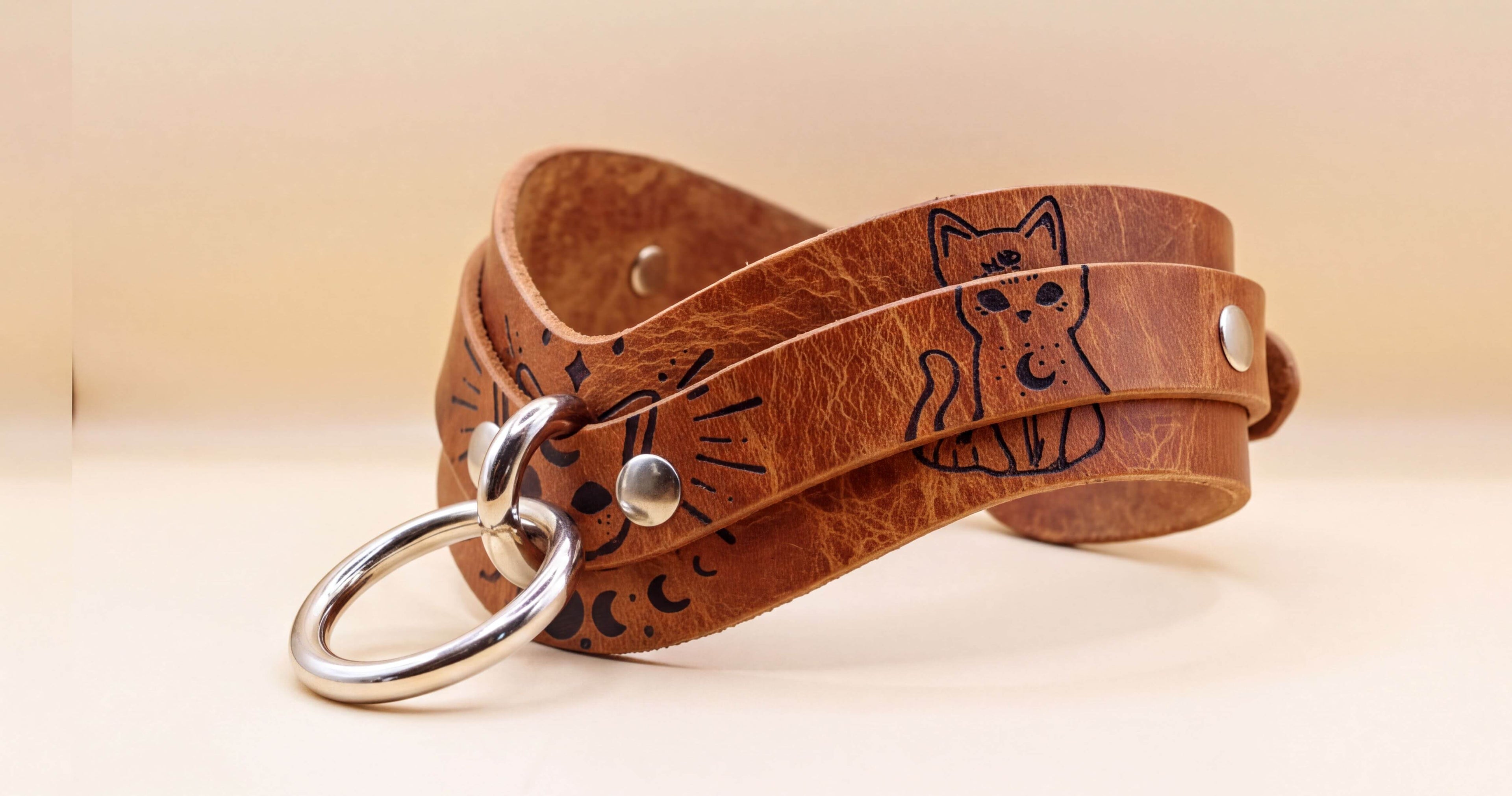A brown leather choker necklace with a cat design and metal rings.