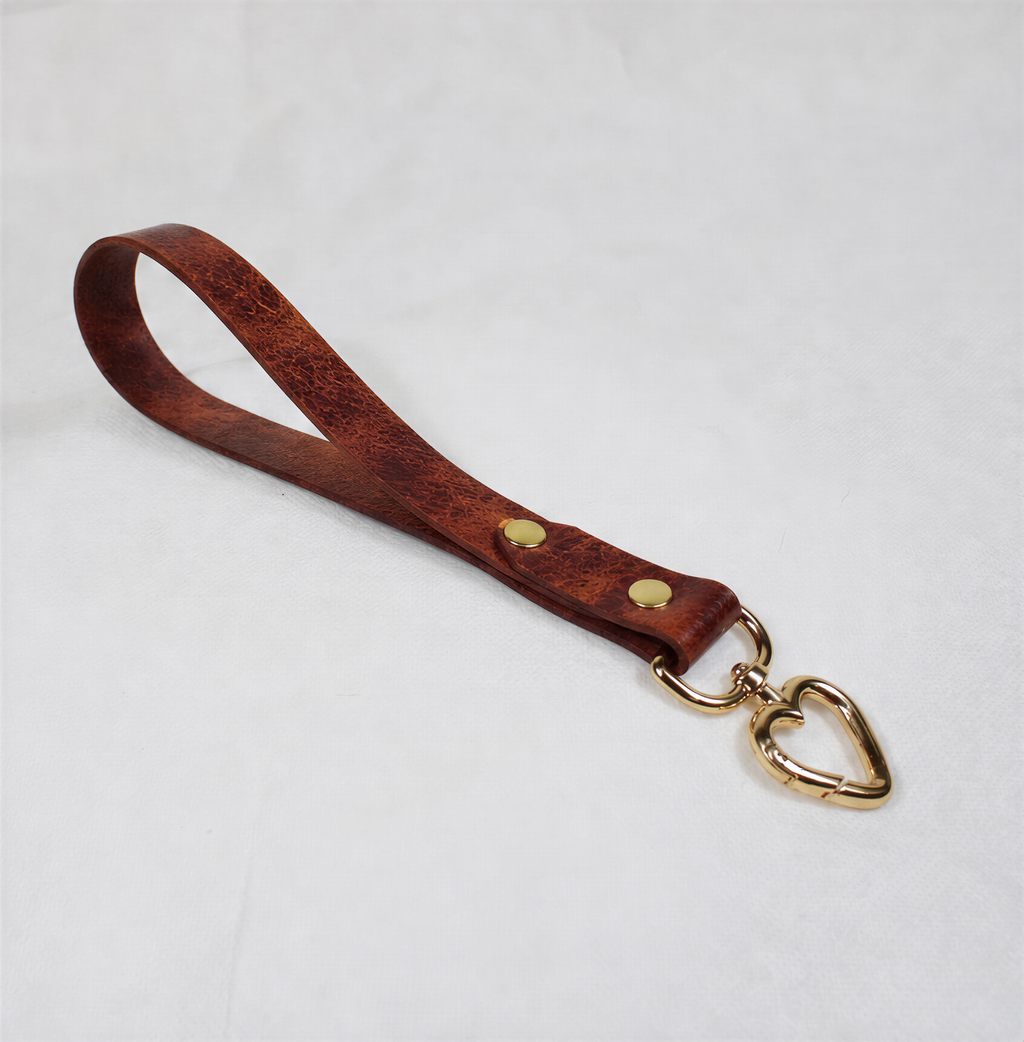 A brown leather strap with a heart-shaped metal clasp attached to it.