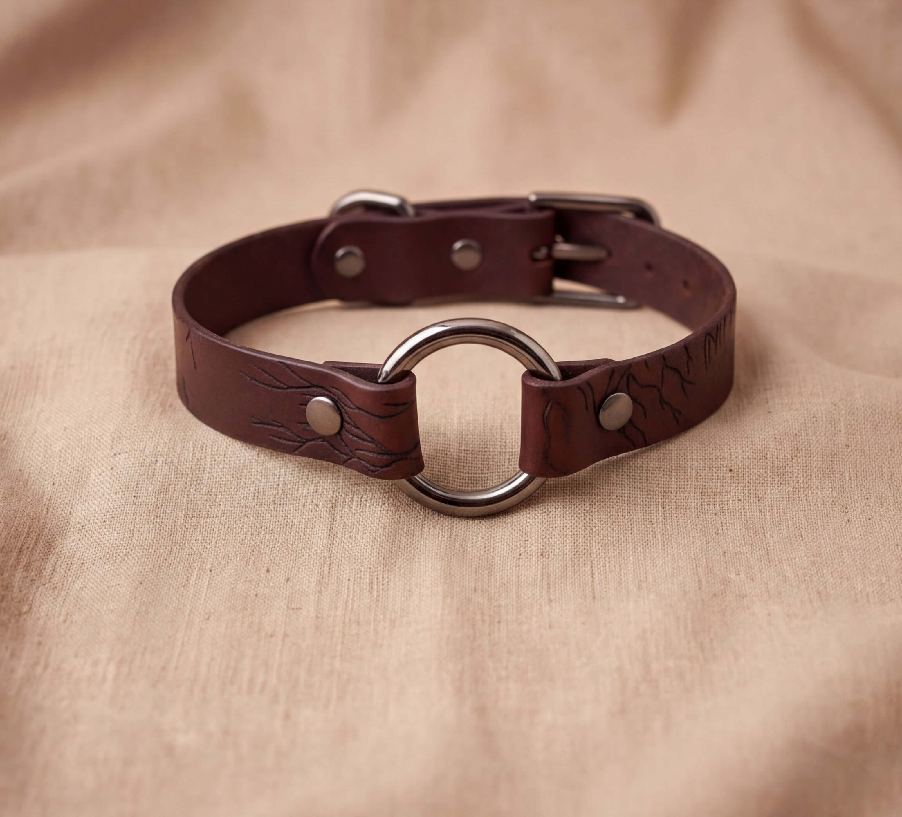 A brown leather choker collar with a metal ring and buckle.