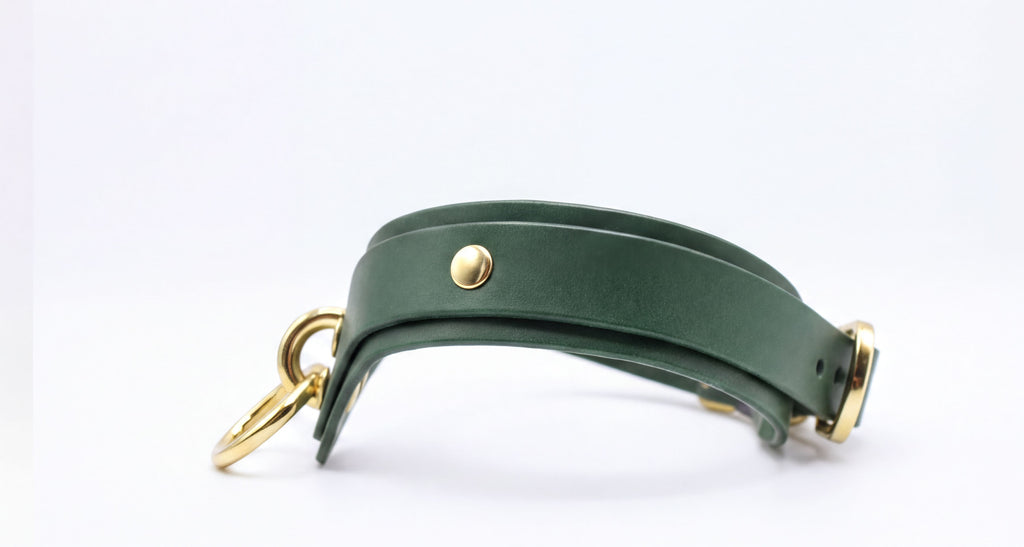 A green leather strap with a gold buckle and ring attached, resting on a white background.
