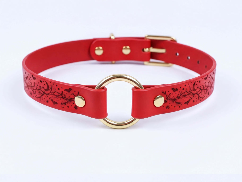 A red leather choker collar with a gold-colored buckle and a circular ring on the front.
