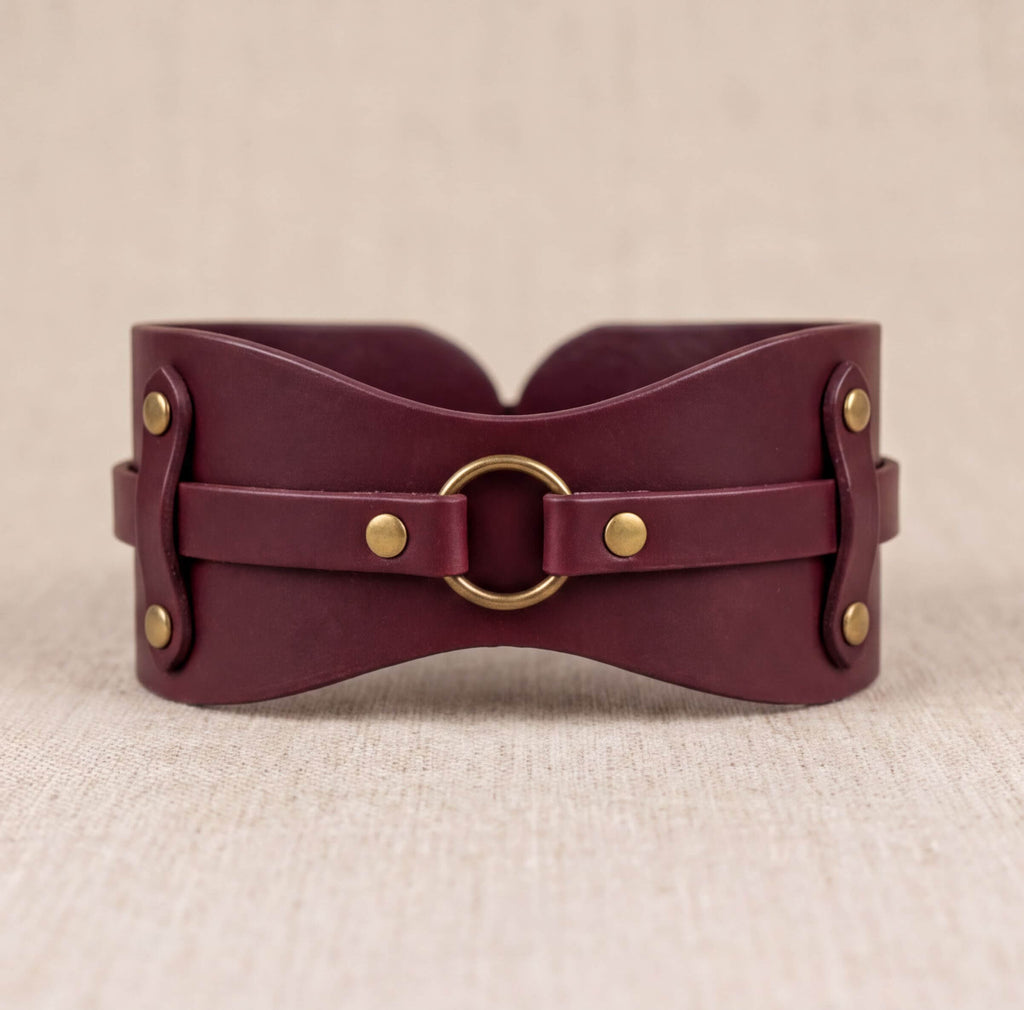 A burgundy leather corset with a brass ring and buckle fastening.
