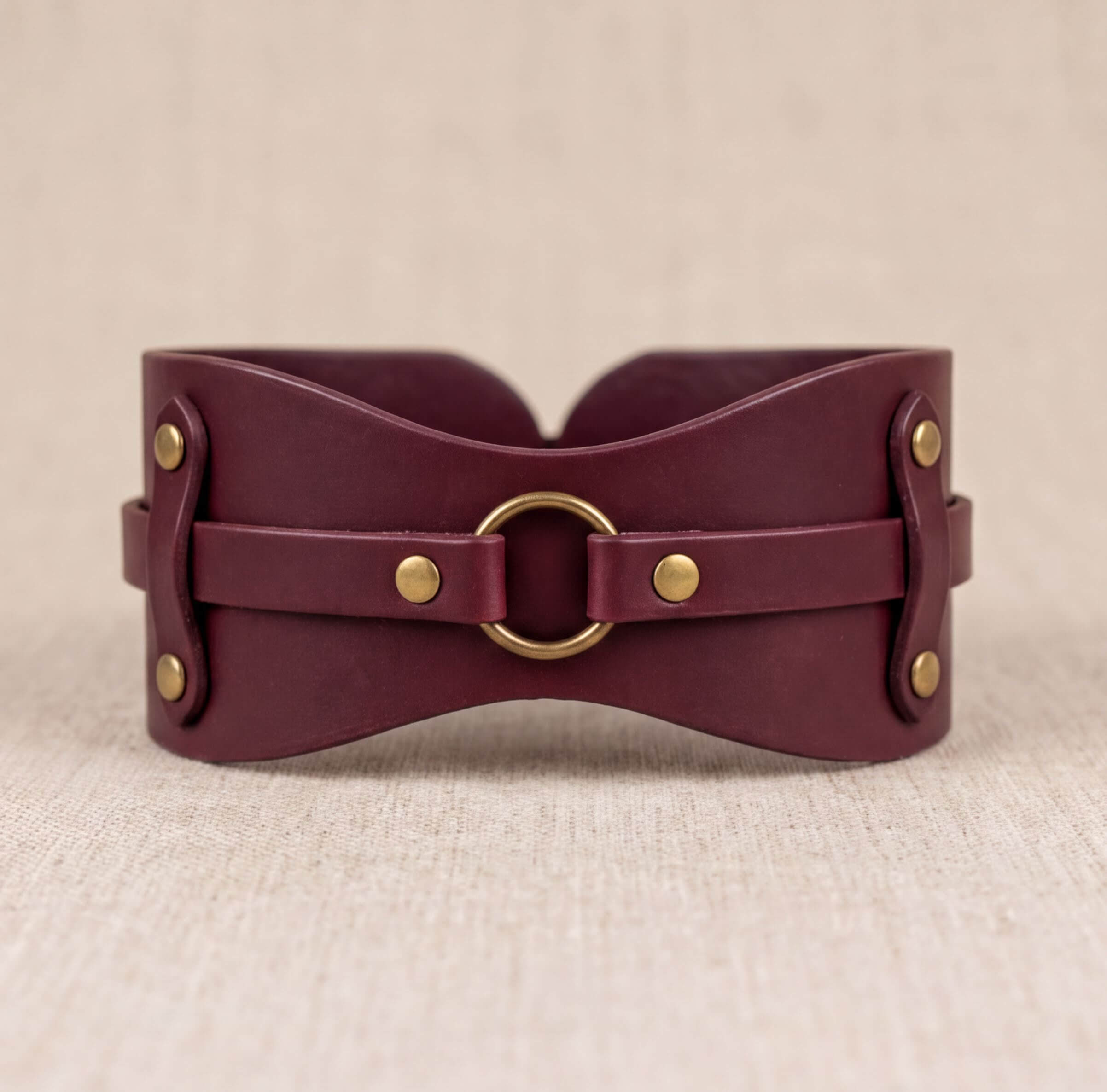 A burgundy leather corset with a brass ring and buckle fastening.