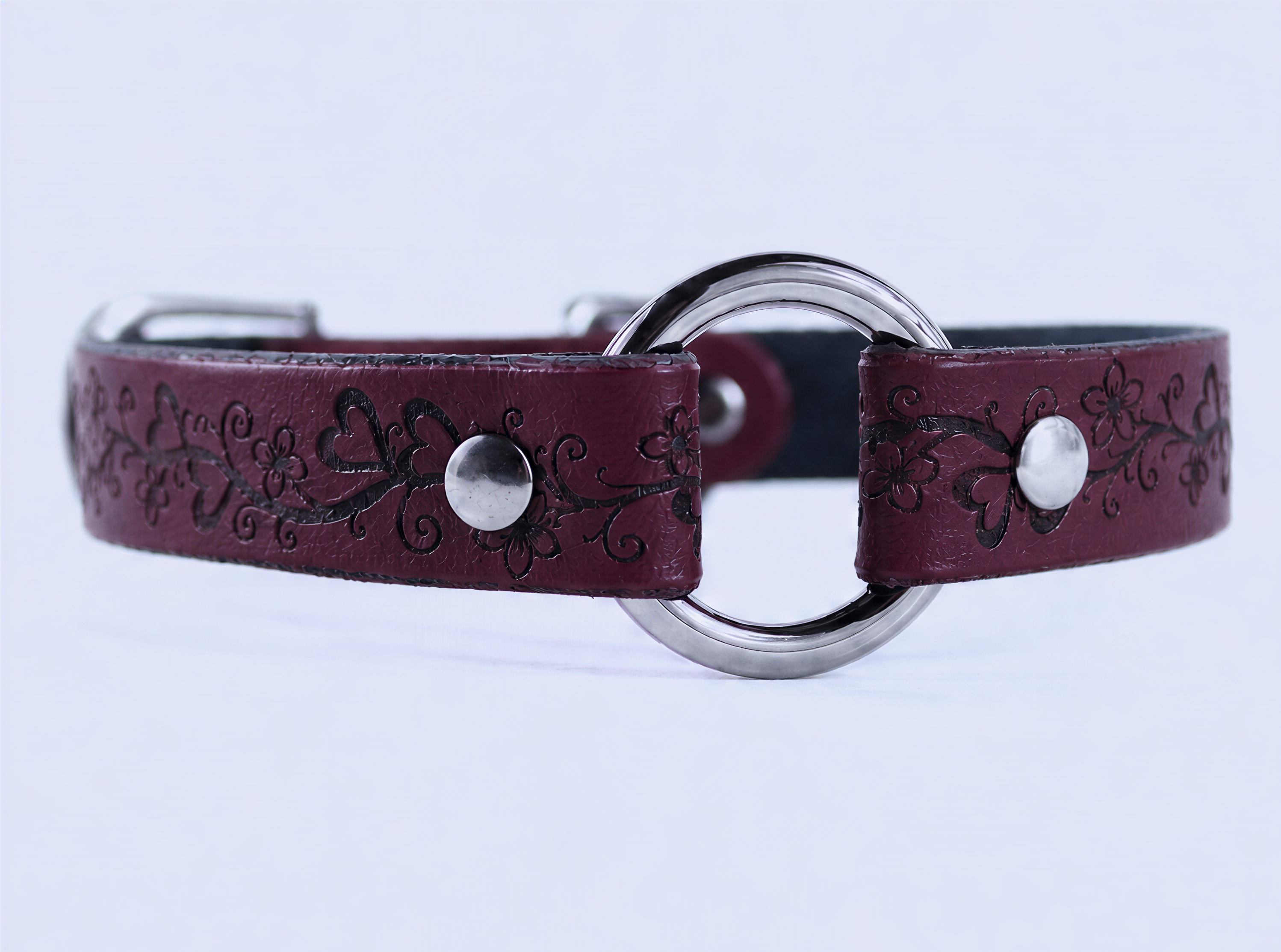 A burgundy leather collar with a circular metal buckle and floral designs.