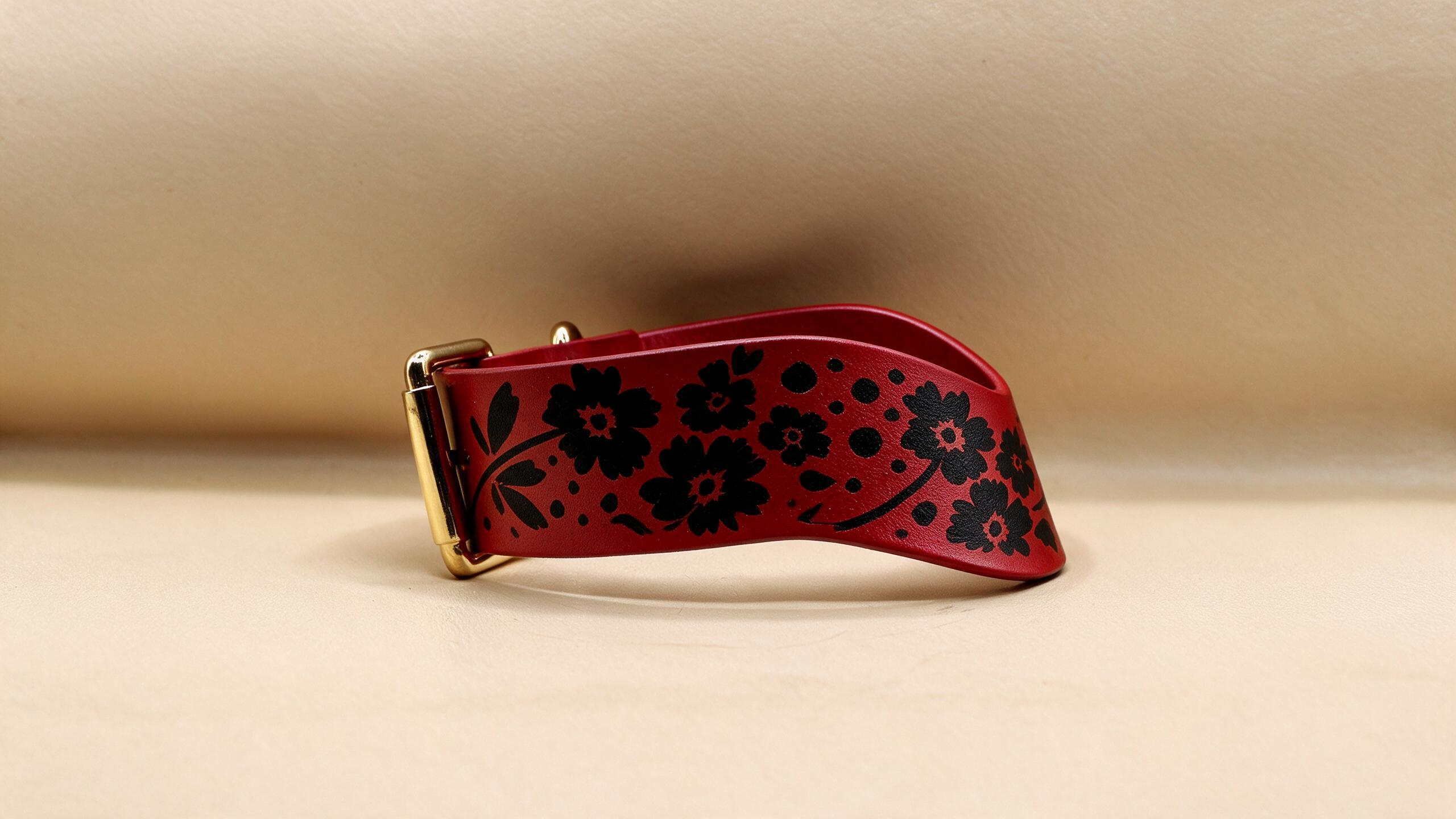 A red leather strap with black floral designs on it.