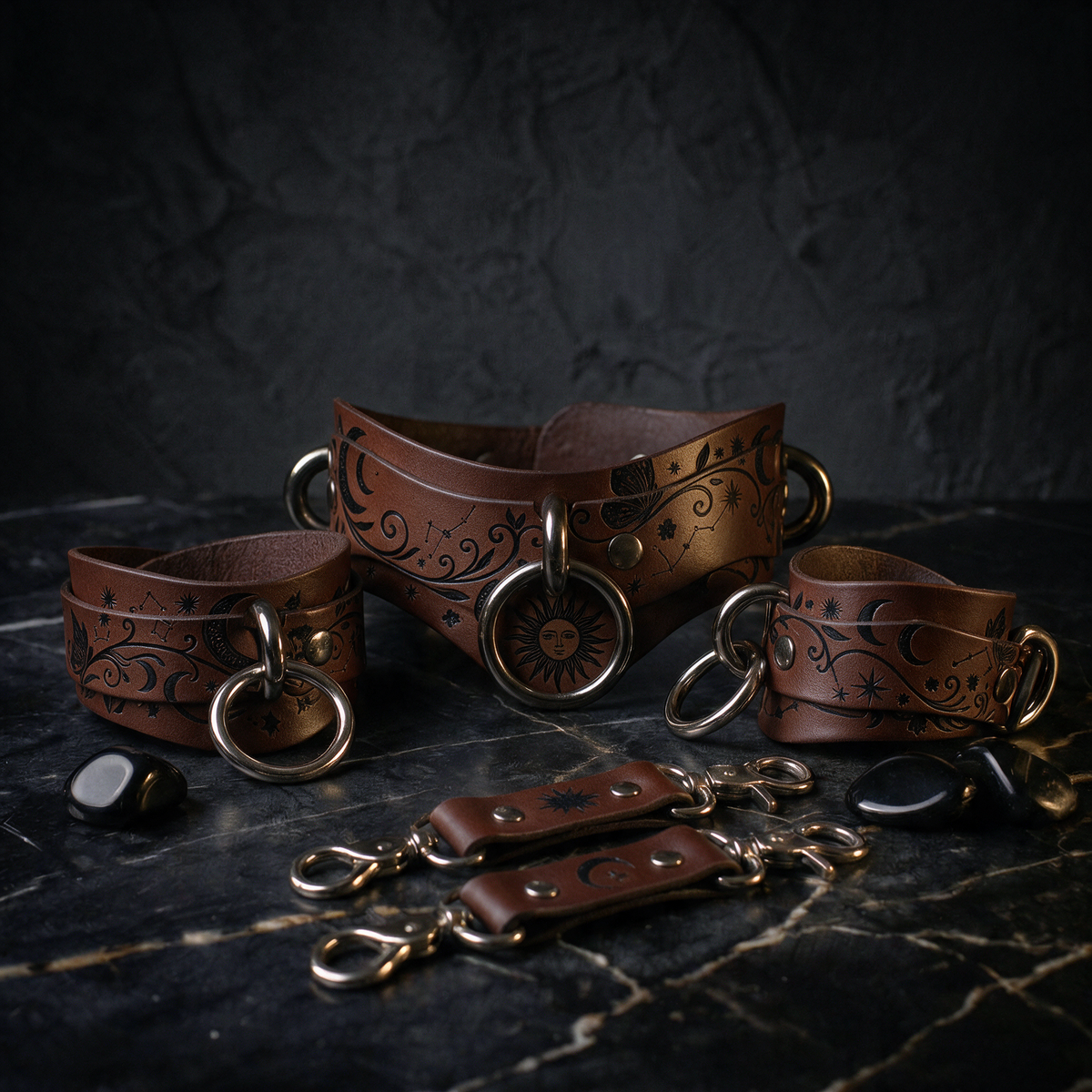 A set of leather choker necklaces and straps with intricate designs, including sun and moon motifs, displayed on a dark surface.