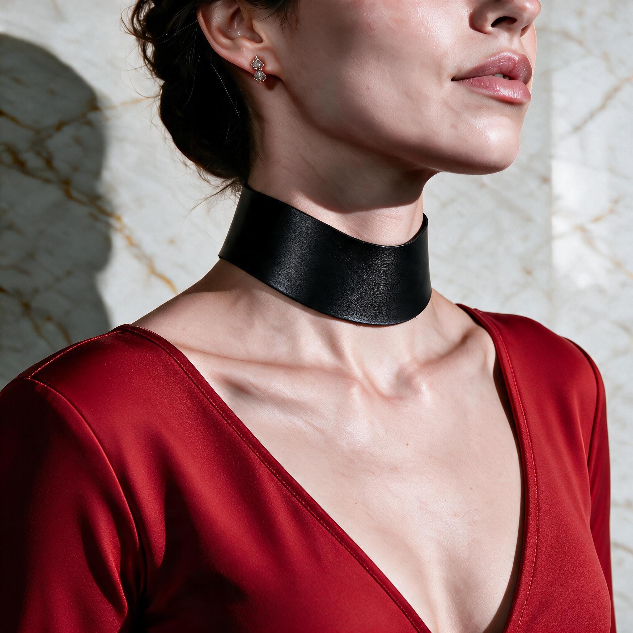A woman wearing a black choker necklace and a red dress stands against a marble wall.
