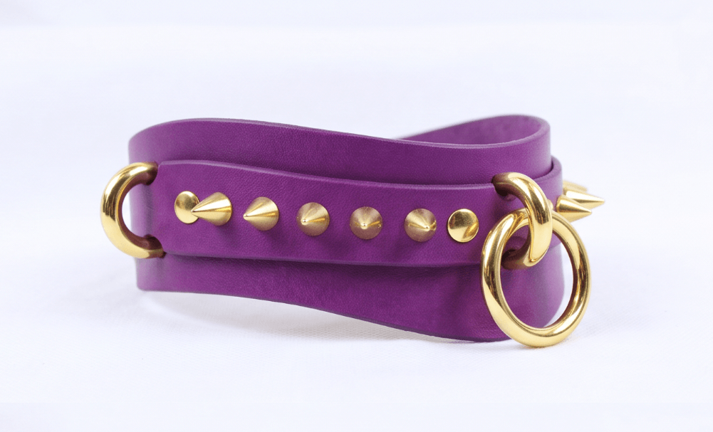 A purple leather choker necklace with gold studs and a gold ring.