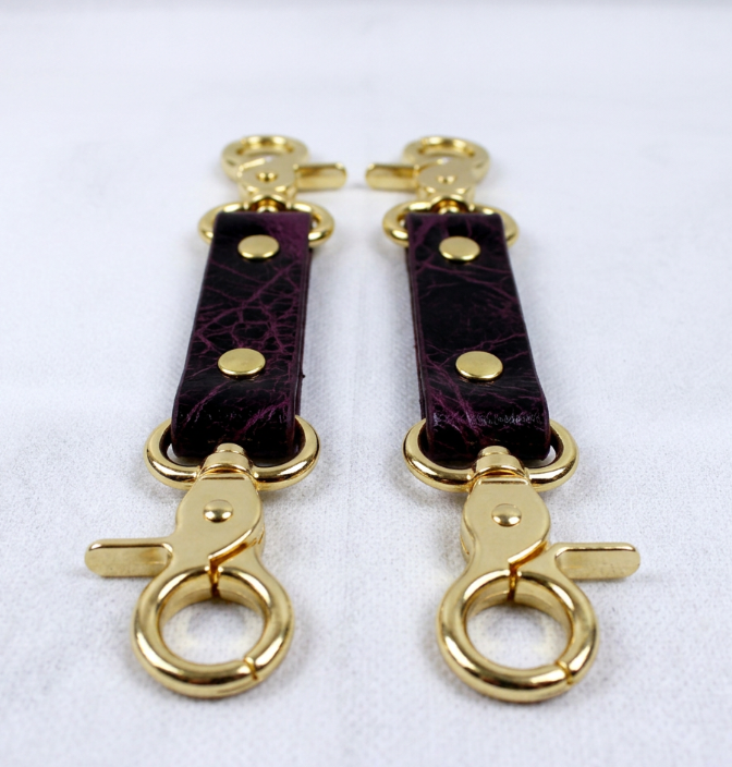 a pair of gold-colored leather straps with gold-colored metal clasps, placed side by side on a white surface.