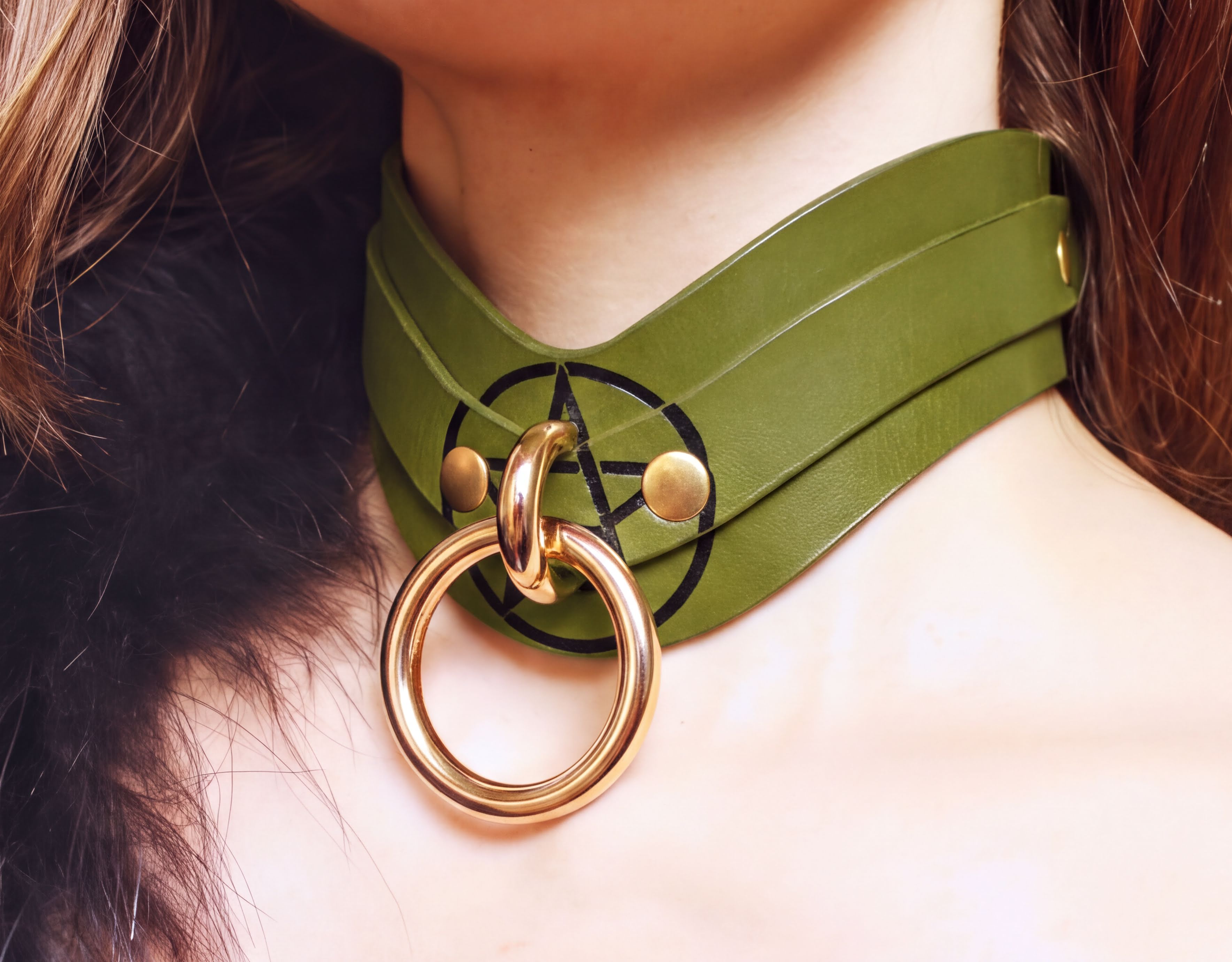 A close-up view of a woman's neck and chest area wearing a green leather choker necklace with a gold-colored ring.