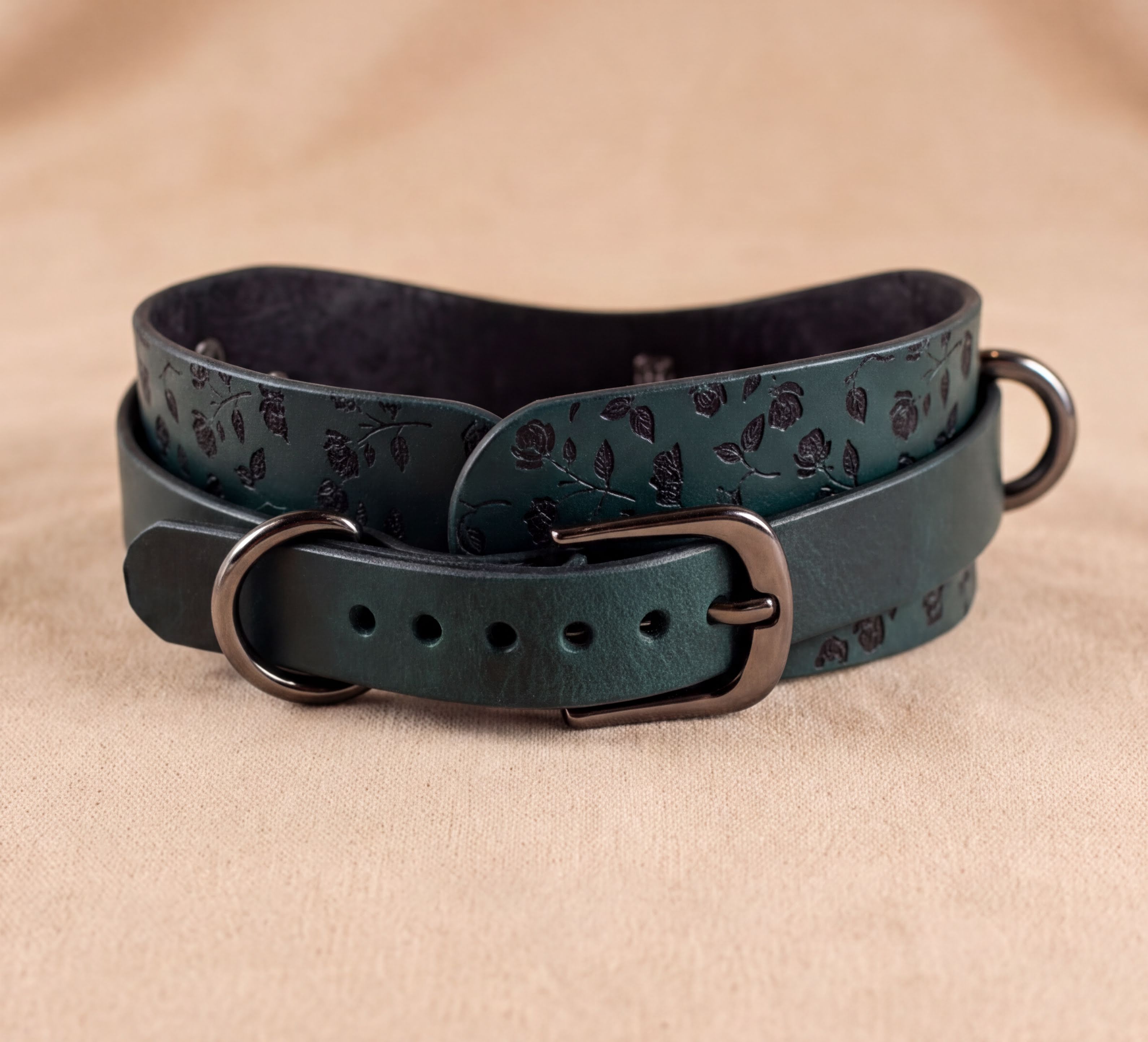 A dark green leather dog collar with a black metal buckle and a black metal ring on the top.