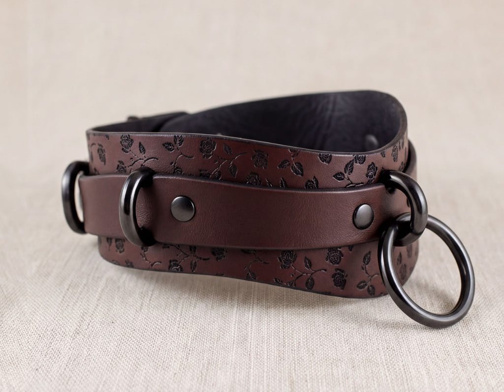A brown leather belt with a floral pattern and two black metal rings on the ends.