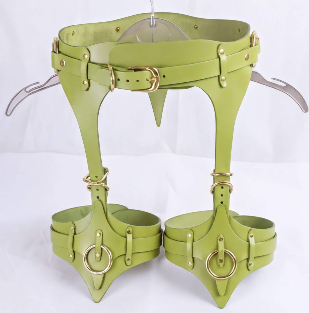 A pair of green leather corsets with metal rings and straps, designed for corsetry or body shaping purposes.