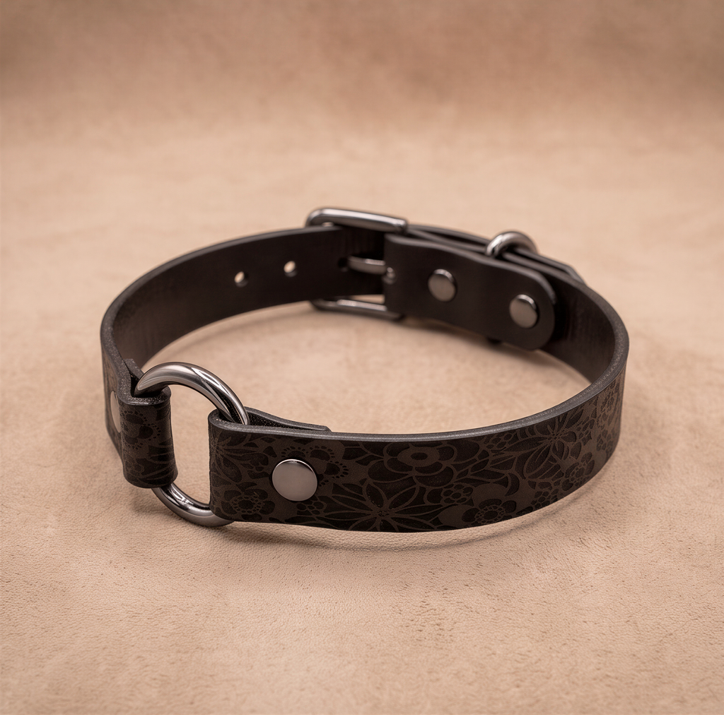 A black leather collar with metal rings and buckles, resting on a beige background.