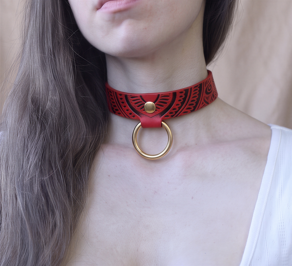 A close-up of a woman's neck wearing a red choker necklace with a gold ring.