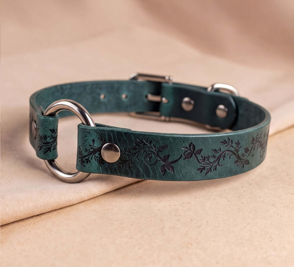 A green leather collar with a floral pattern and metal rings is displayed on a beige fabric background.