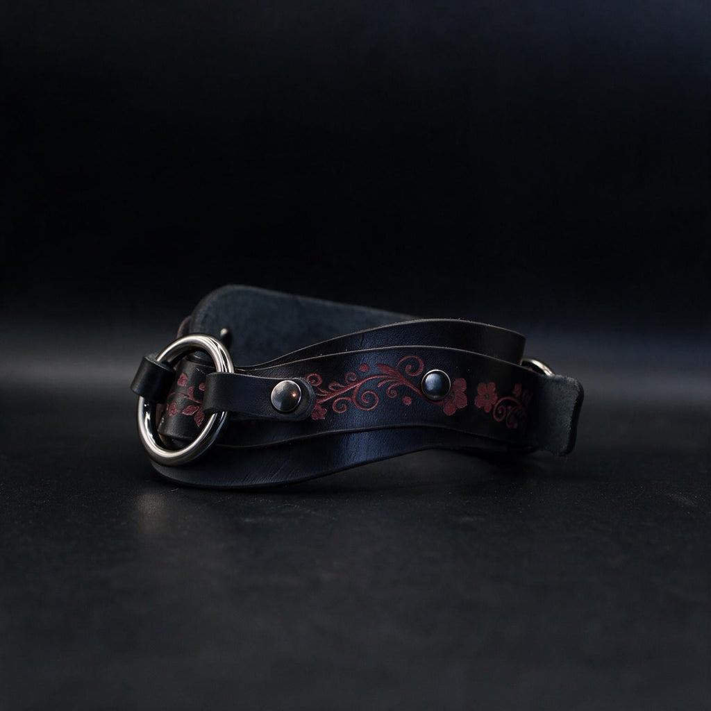 A black leather belt with a silver buckle and floral designs on the band is shown against a dark background.
