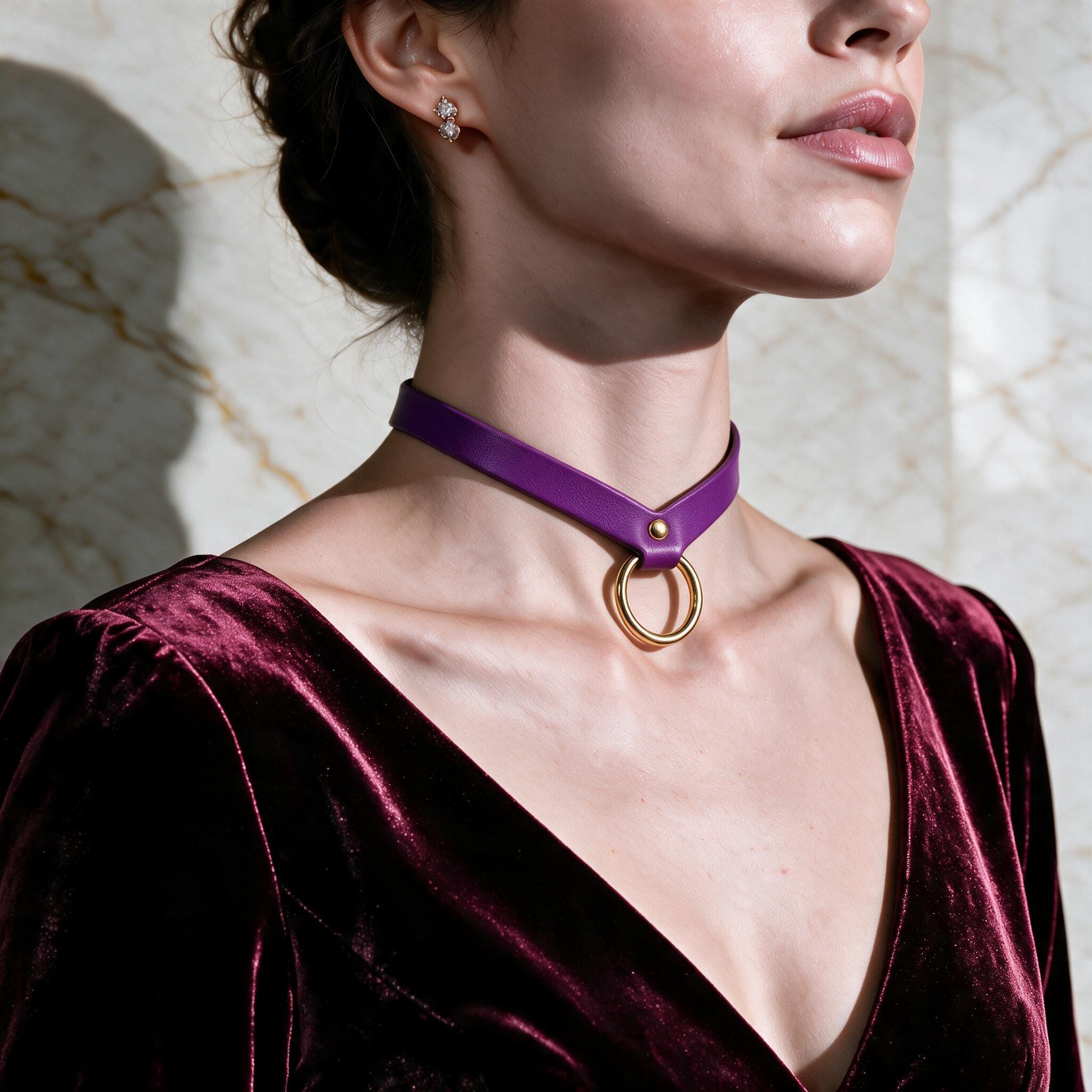 A woman wearing a purple choker necklace with a gold ring is shown in a close-up shot against a marble background.
