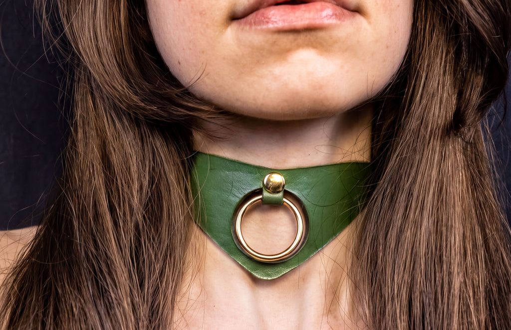 A close-up of a woman's neck and chin wearing a green choker necklace with a gold ring.