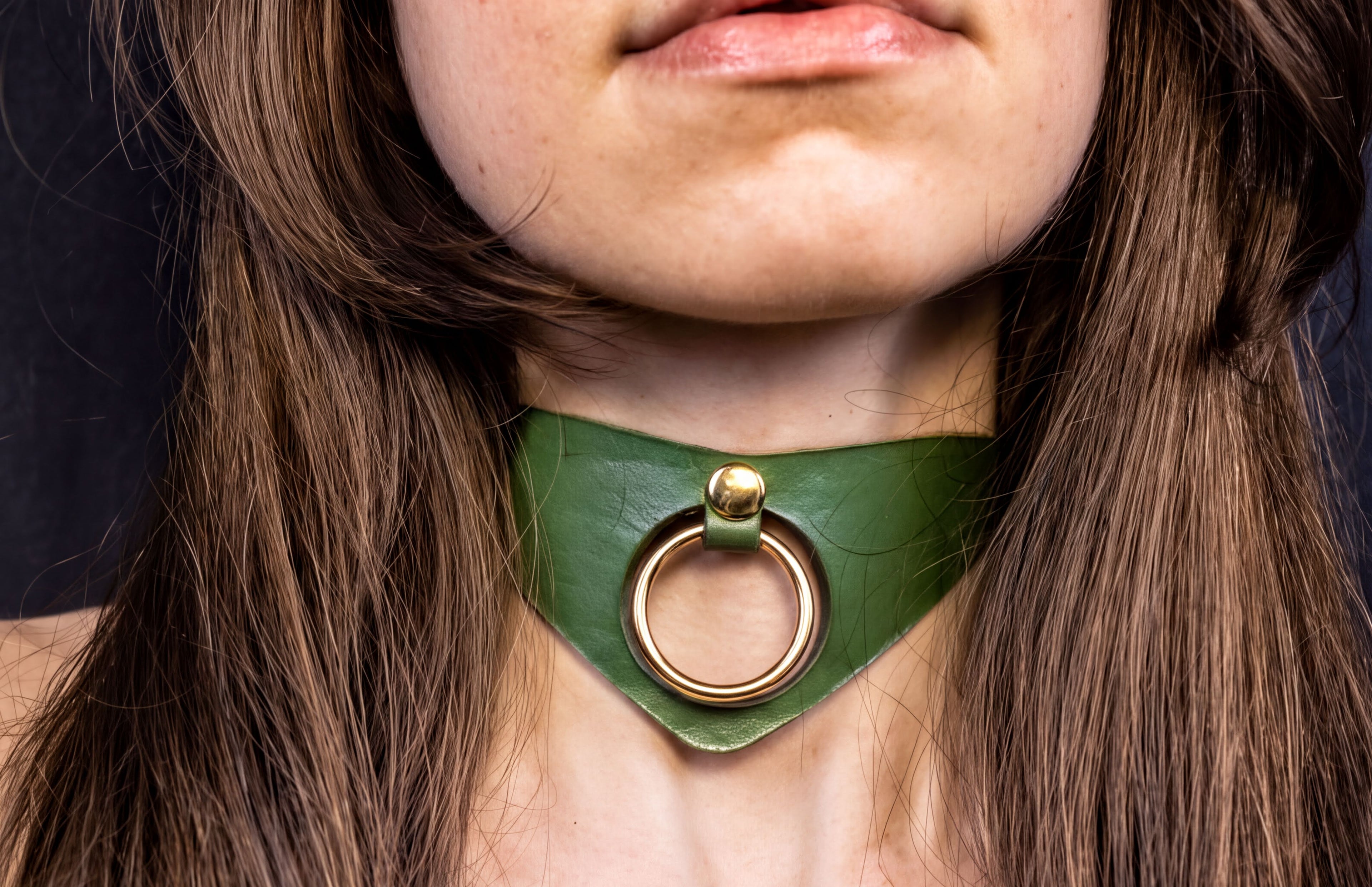 A close-up of a woman's neck and chin wearing a green choker necklace with a gold ring.