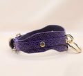 A purple leather strap with a gold-colored buckle, featuring a wave pattern design.