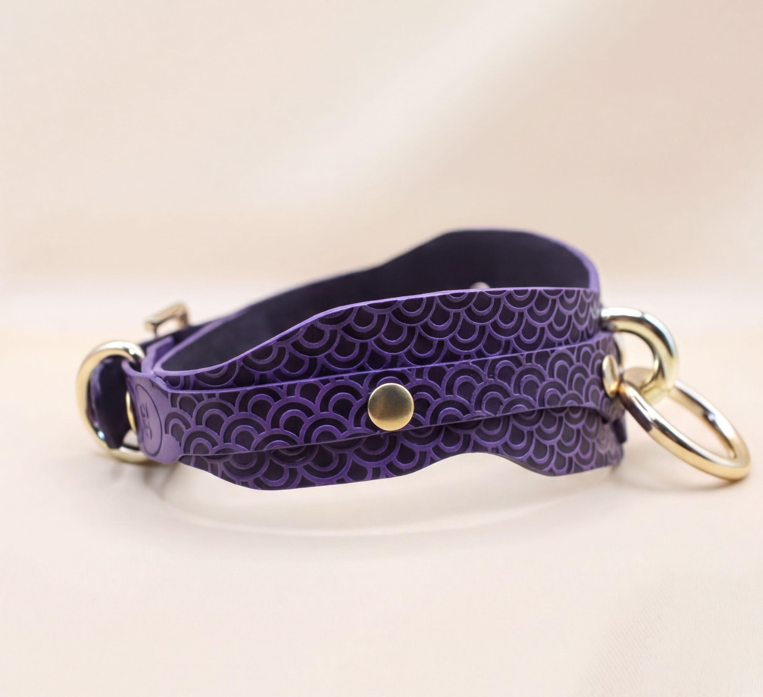 A purple leather strap with a gold-colored buckle, featuring a wave pattern design.
