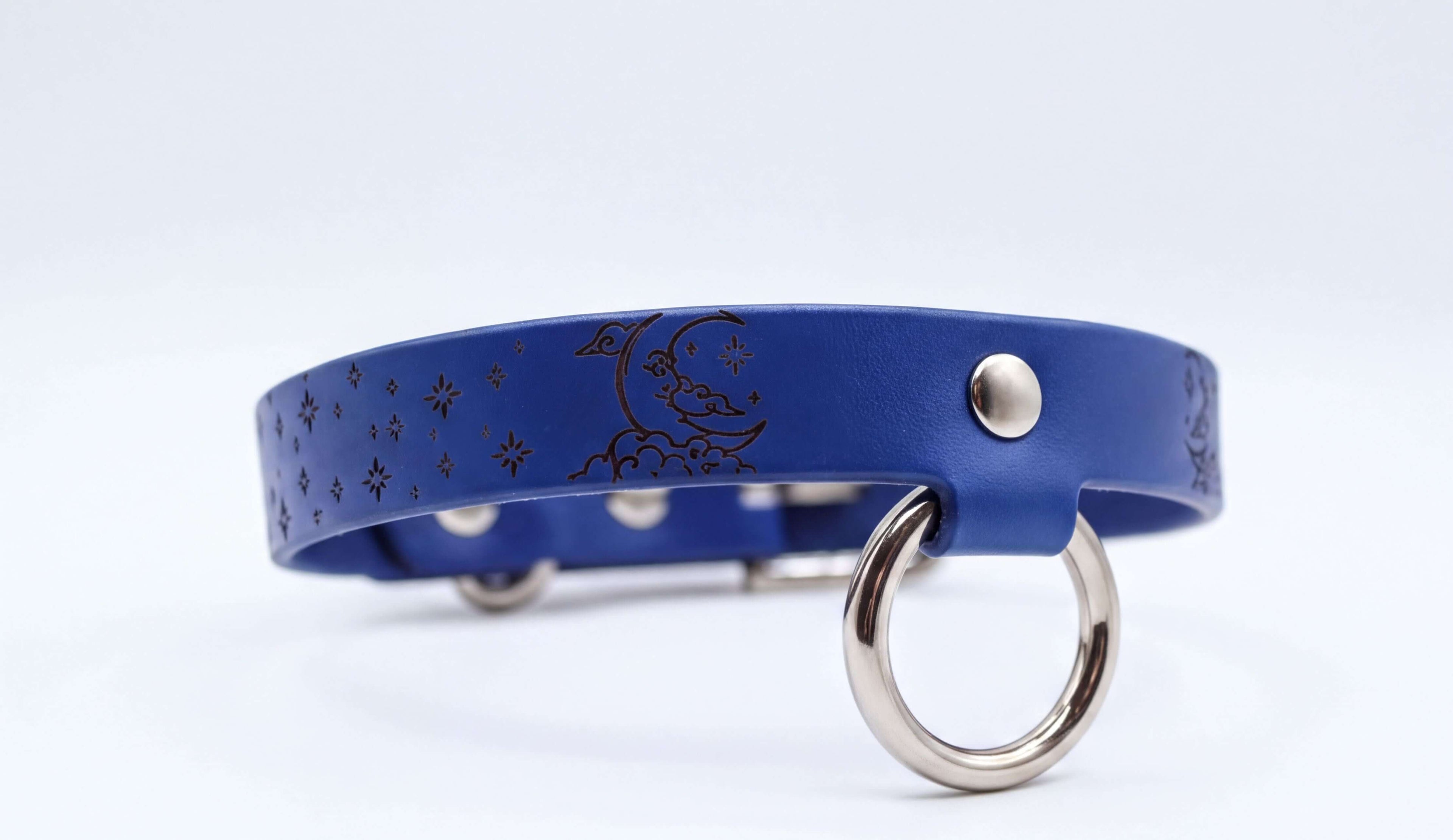 A blue leather collar with a moon and star design on it, featuring a metal ring and buckle.