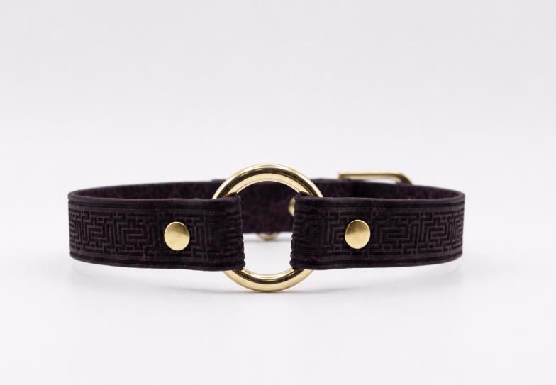 A dark purple leather collar with a gold-colored metal ring and two gold-colored metal fasteners.