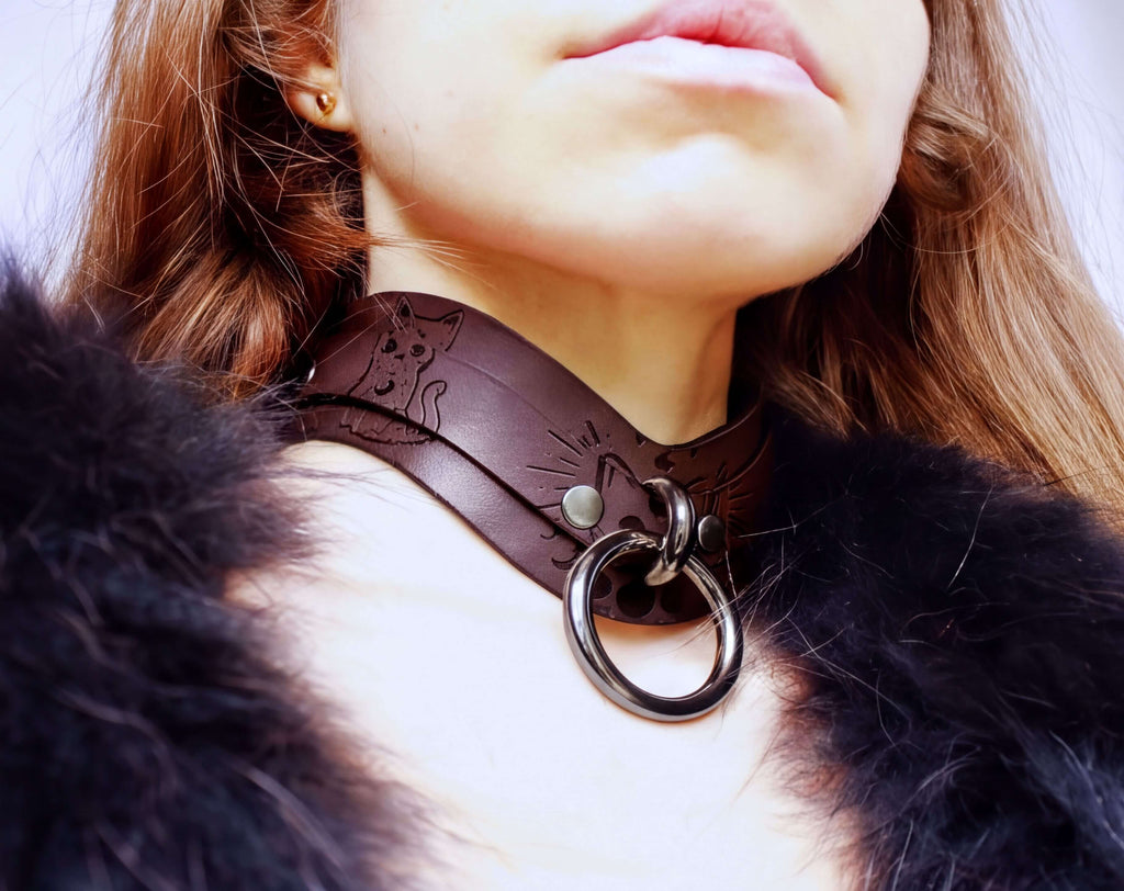 A close-up of a person wearing a brown leather choker necklace with a metal ring and a fur collar.