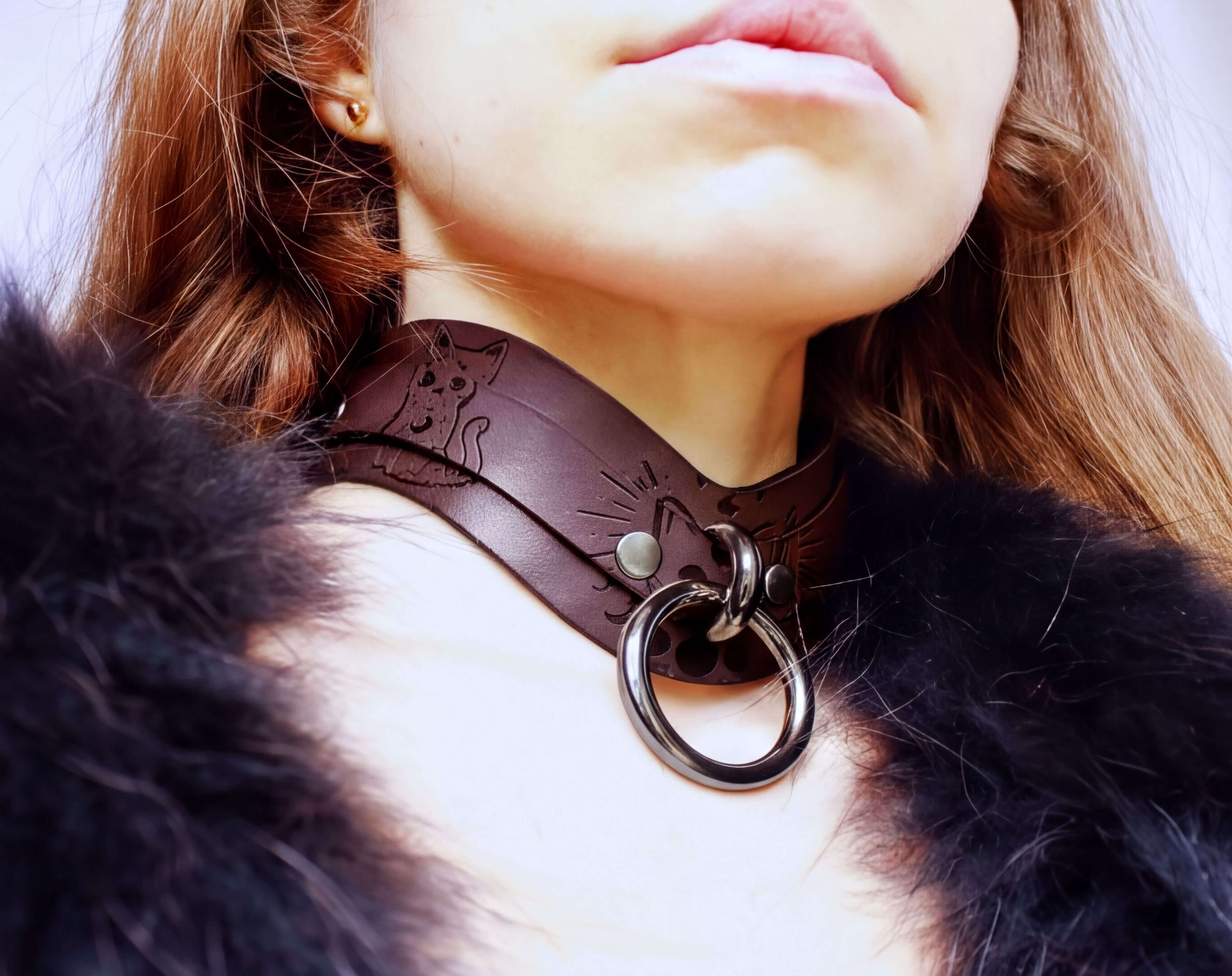 A close-up of a person wearing a brown leather choker necklace with a metal ring and a fur collar.