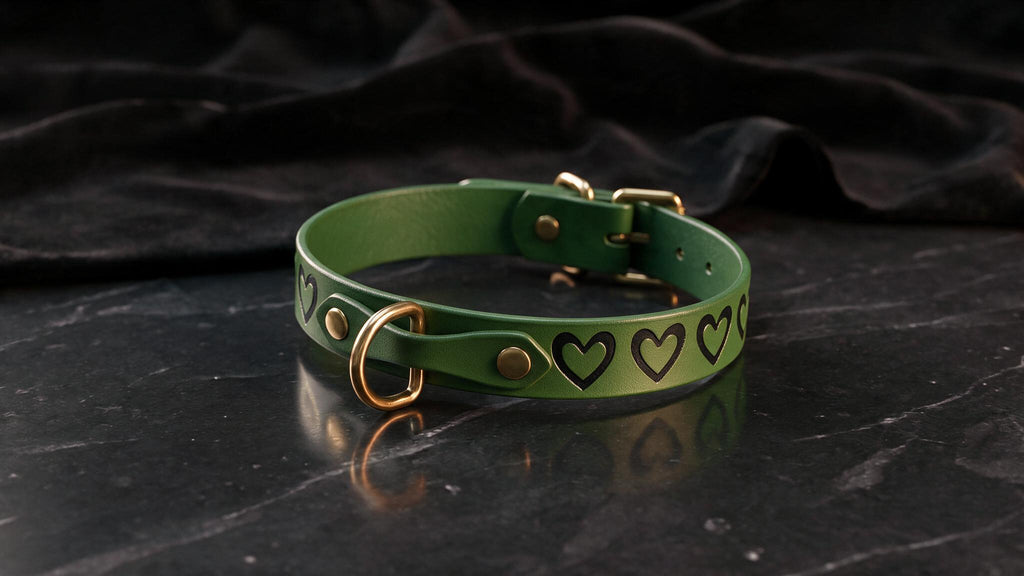A green leather collar with heart-shaped embellishments is displayed on a black marble surface.