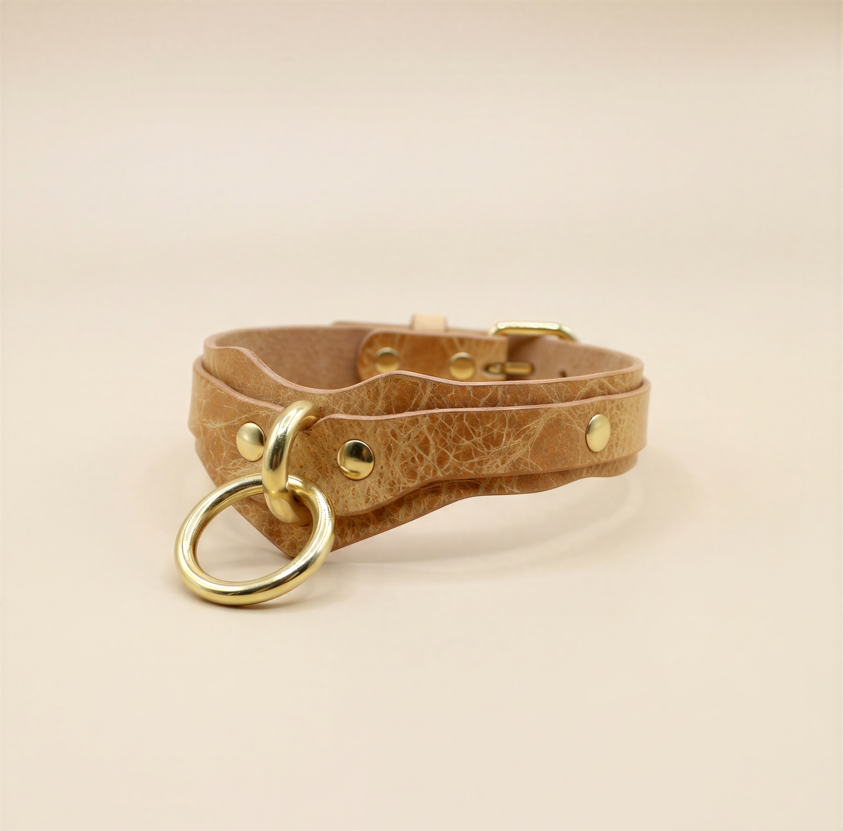 A tan leather choker necklace with a gold-colored metal ring and buckle.