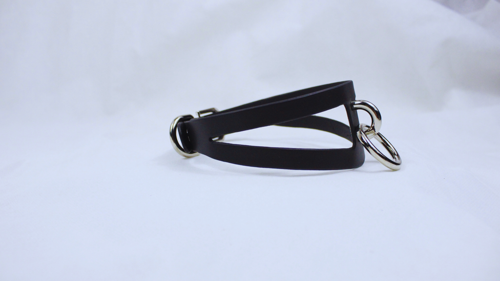 A black leather choker necklace with metal rings and a buckle is shown against a white background.
