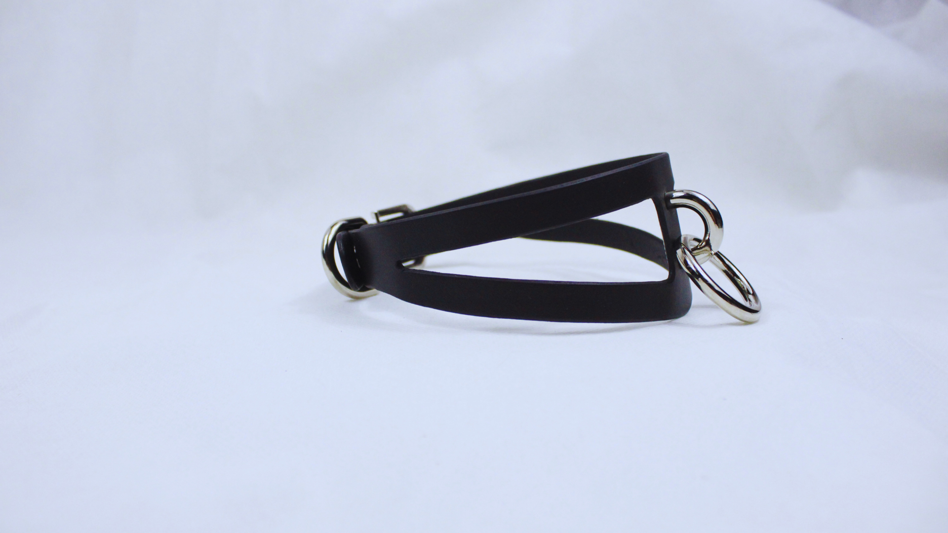A black leather choker necklace with metal rings and a buckle is shown against a white background.