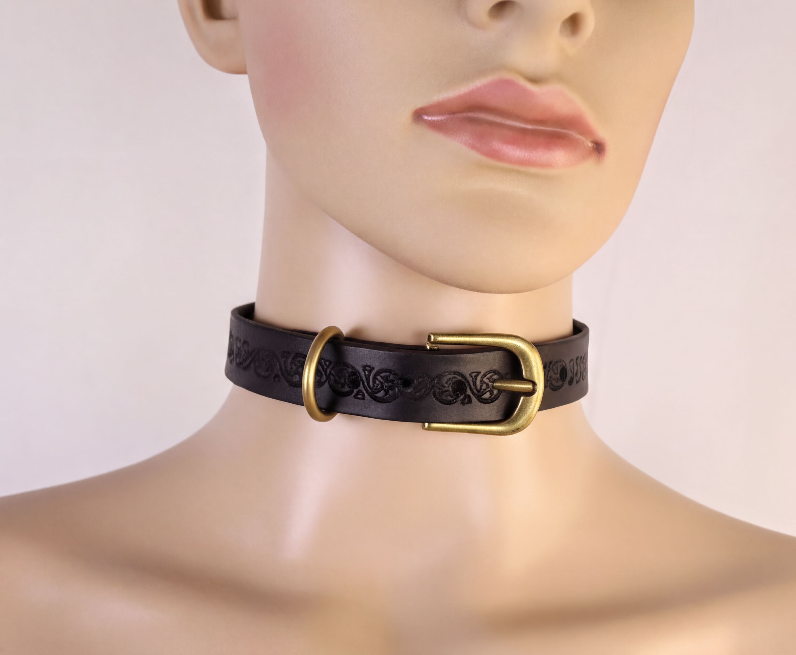 A mannequin head wearing a black leather choker necklace with a brass buckle.