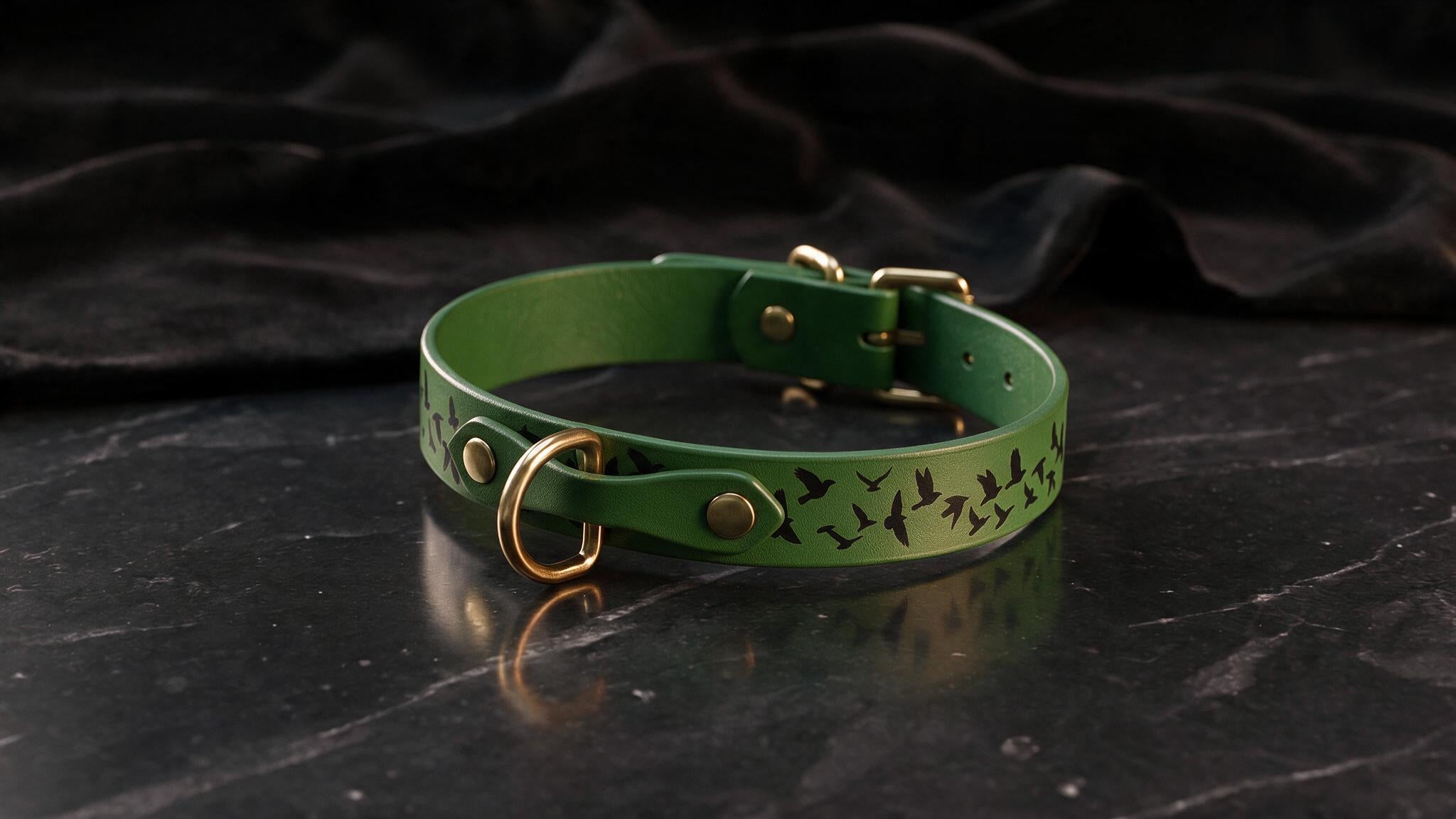 A green leather collar with a bird design on it, placed on a black marble surface.