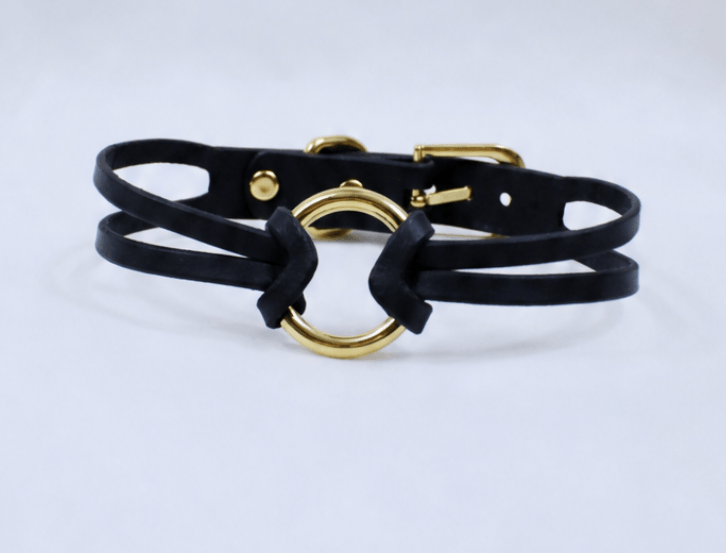 A black leather choker necklace with a gold-colored circular clasp.