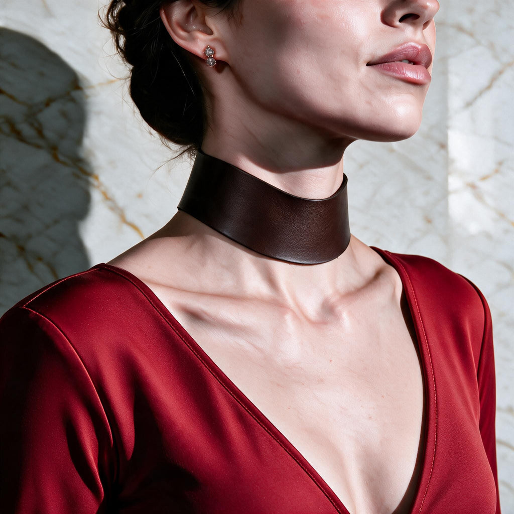 A woman wearing a red dress with a choker necklace stands against a marble wall.