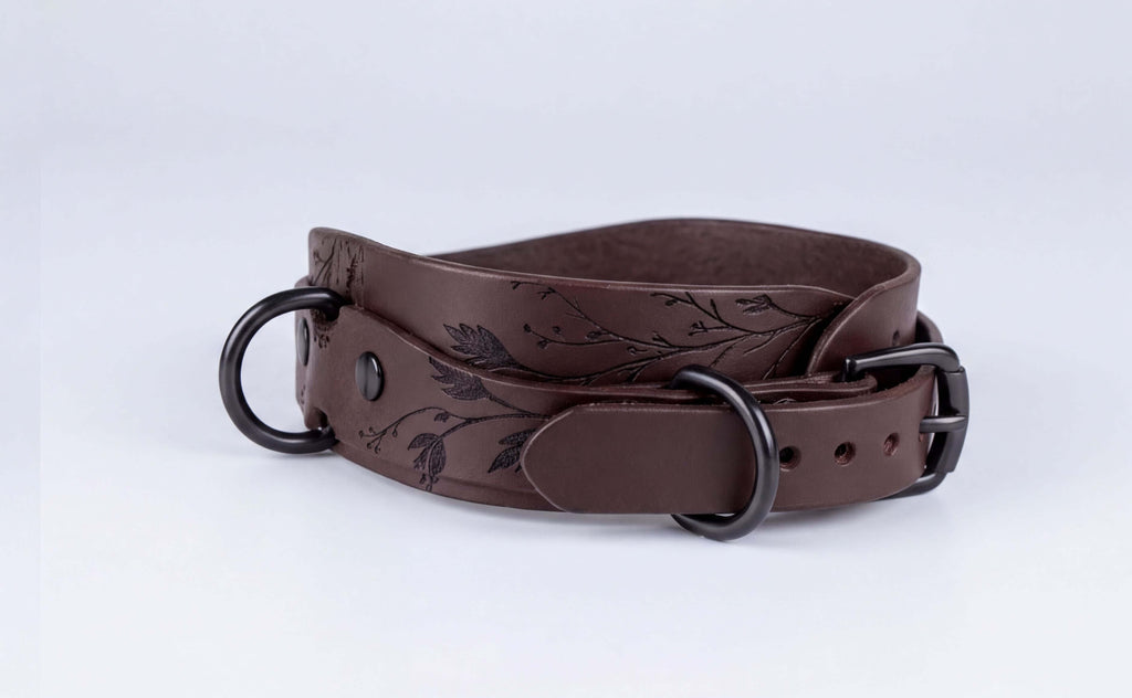 A brown leather belt with a floral design on the buckle and two black metal buckles.