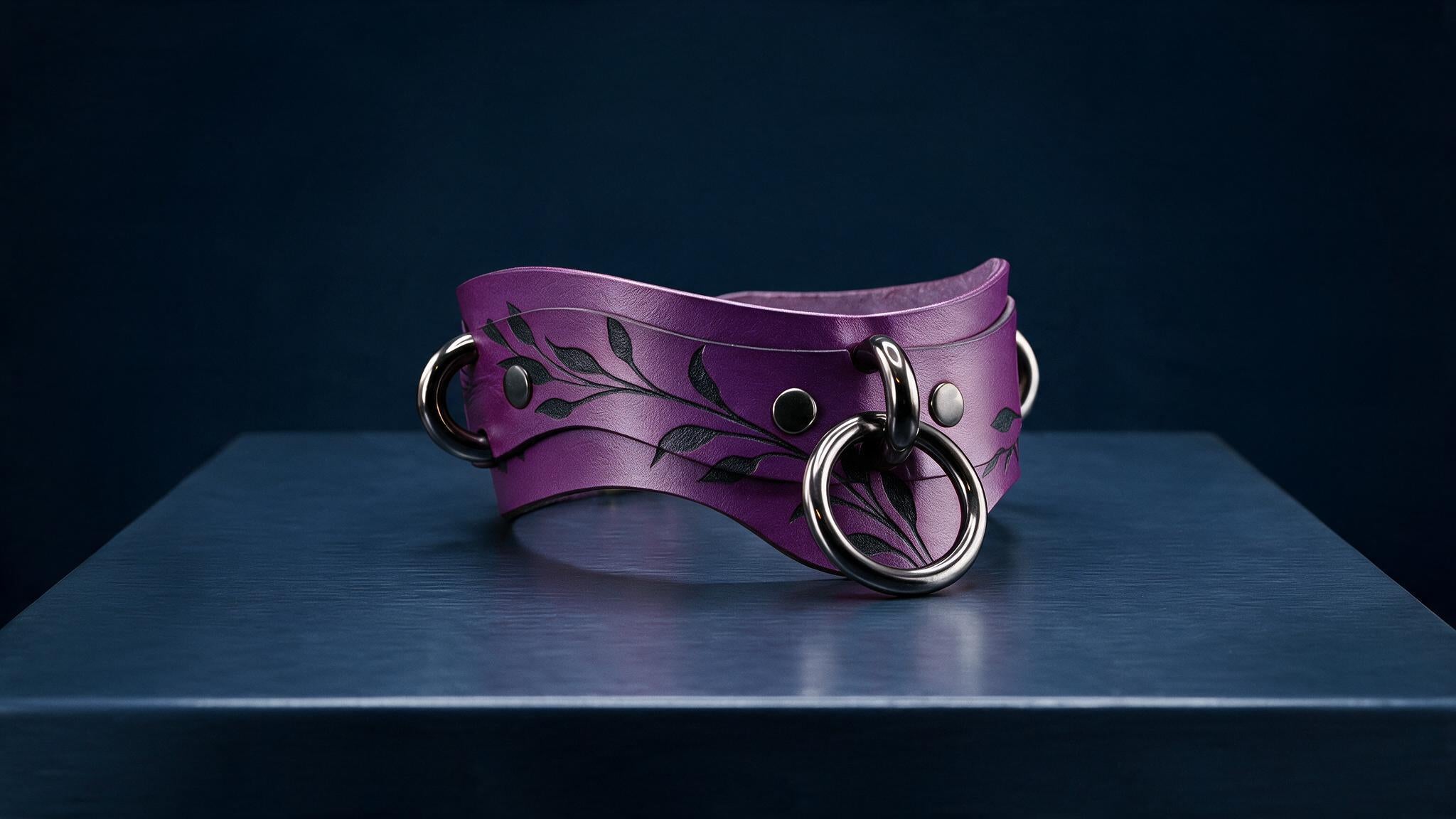 A purple leather choker necklace with a leaf design and metal rings is displayed on a dark surface.