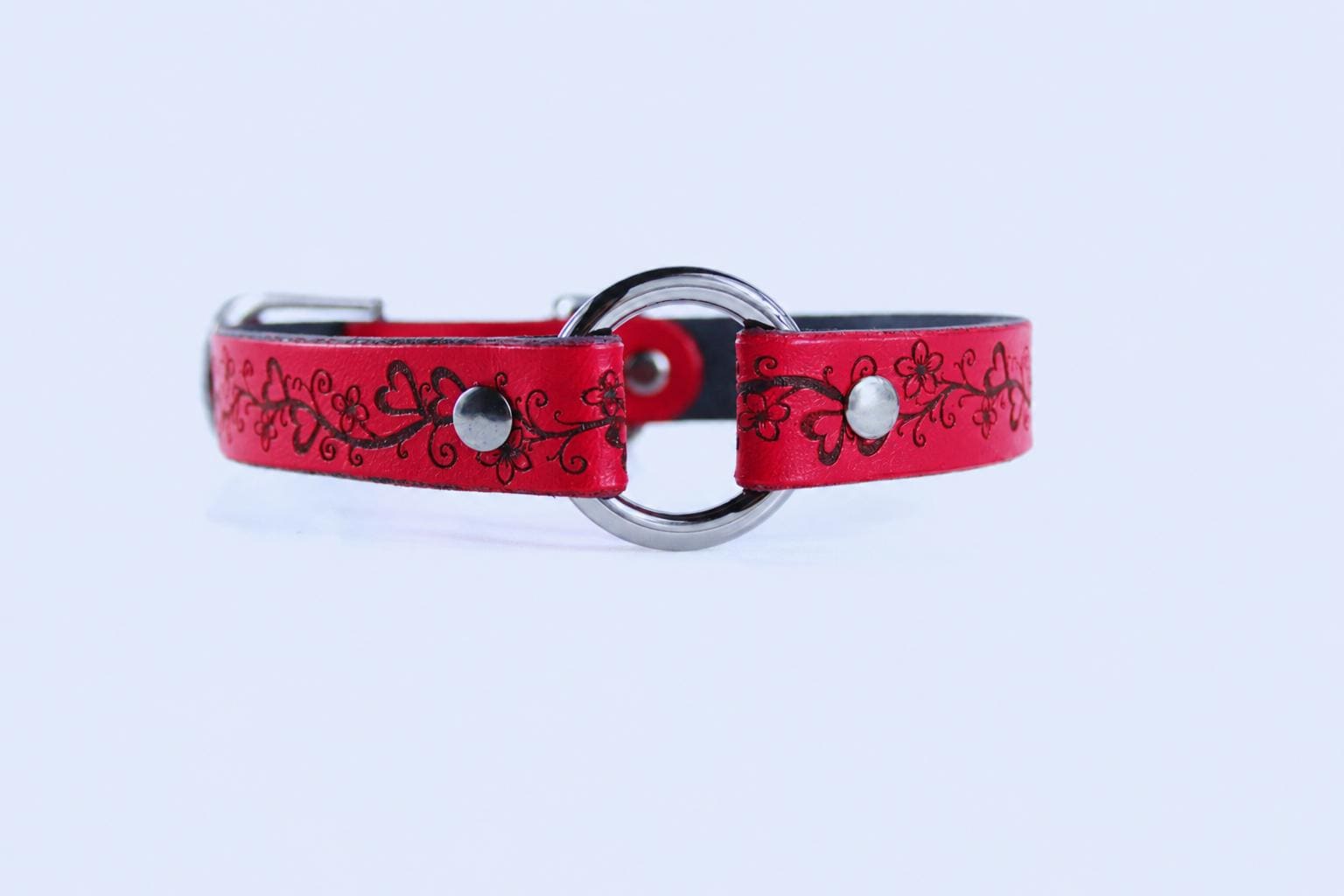A red leather collar with a floral design and metal ring.