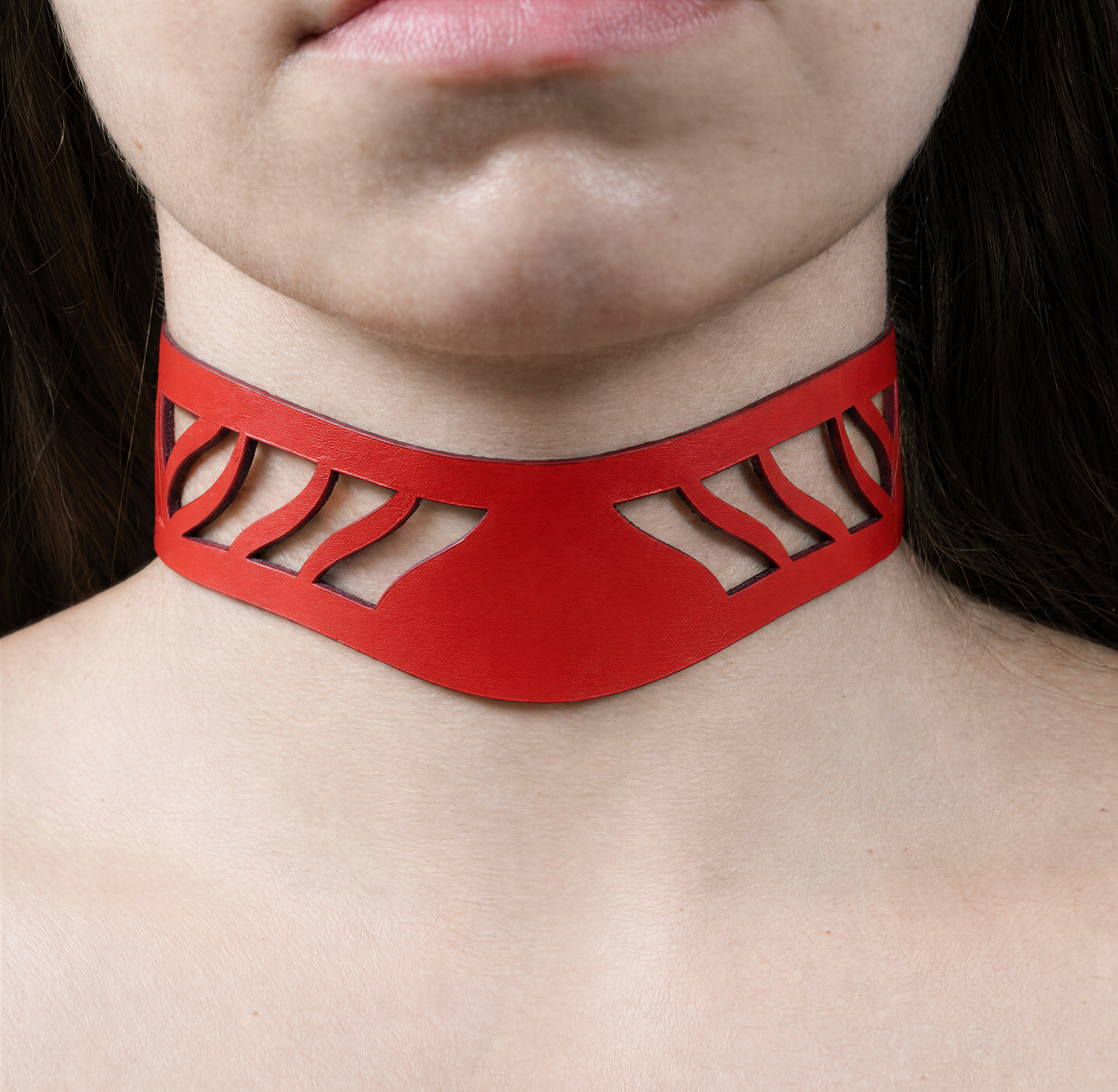 A close-up of a person's neck and chest area wearing a red choker necklace with a unique cutout design.